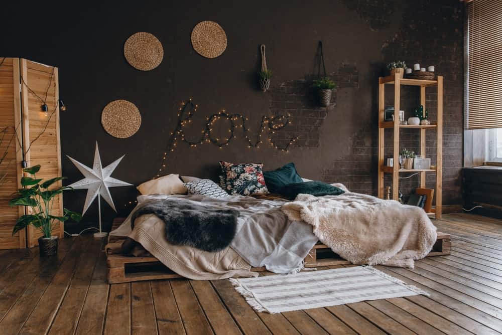 这间工业风格的主卧室有一种浪漫的氛围，平台床架由托盘板条箱制成，与破旧的硬木地板融合在一起，与房间的木结构相辅相成，在深灰色的墙壁衬托下脱颖而出。