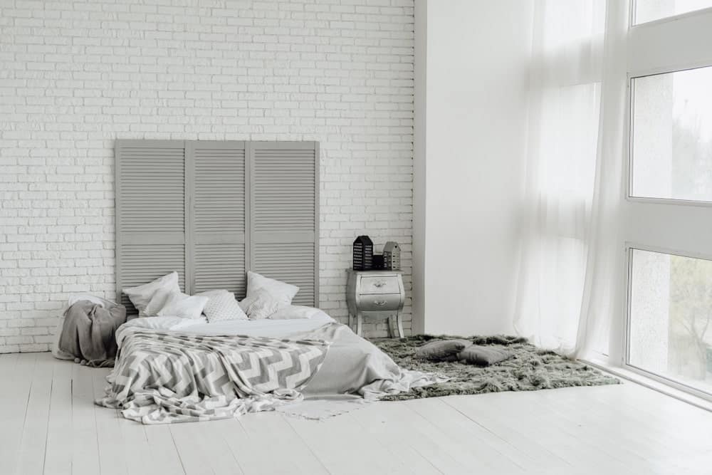 纯窗帘玻璃窗带来了充足的自然采光，使白色纹理的砖墙图案更加明亮。在浅灰色地板上，木质隔板作为平台床的高床头板。