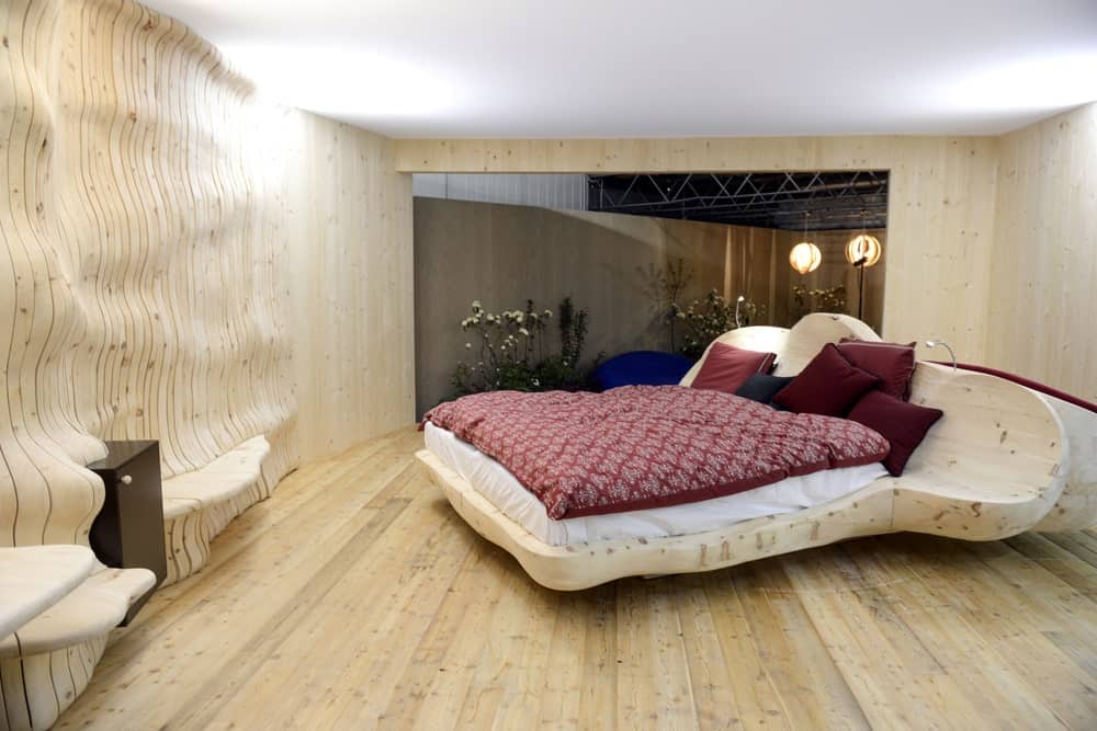 这个工业风格的卧室有轻质硬木地板，与独特的定制床架相融合，具有流体形状。与这种美学相匹配的是相同材料和色调的墙壁，它们似乎在流动和涟漪中创造出书架。