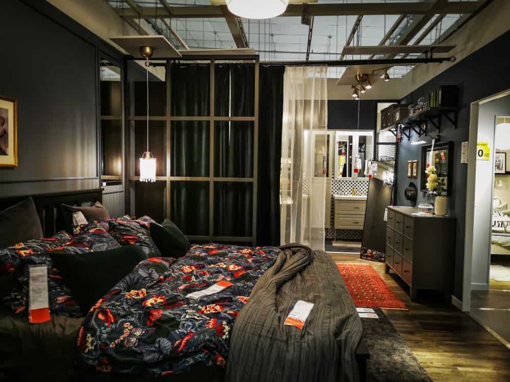 这间工业风格的卧室铺着灰色色调的硬木地板，与传统床的床单、梳妆台和架子相匹配。这是暗灰色的墙壁和吊灯照亮。