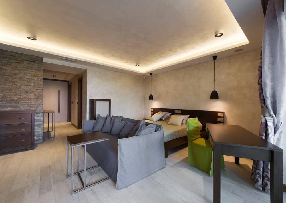 主卧室有一个流行的床上设置和一个现代的灰色沙发与现代表,设置在房间的华丽的托盘天花板匹配的墙上。