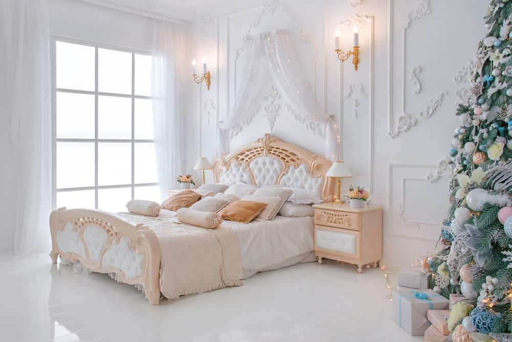 破旧别致的主卧室设有优雅的床设置，周围环绕着优雅的白色装饰墙壁，由壁灯照明。房间还铺着白色硬木地板，窗户上有可爱的白色窗帘。