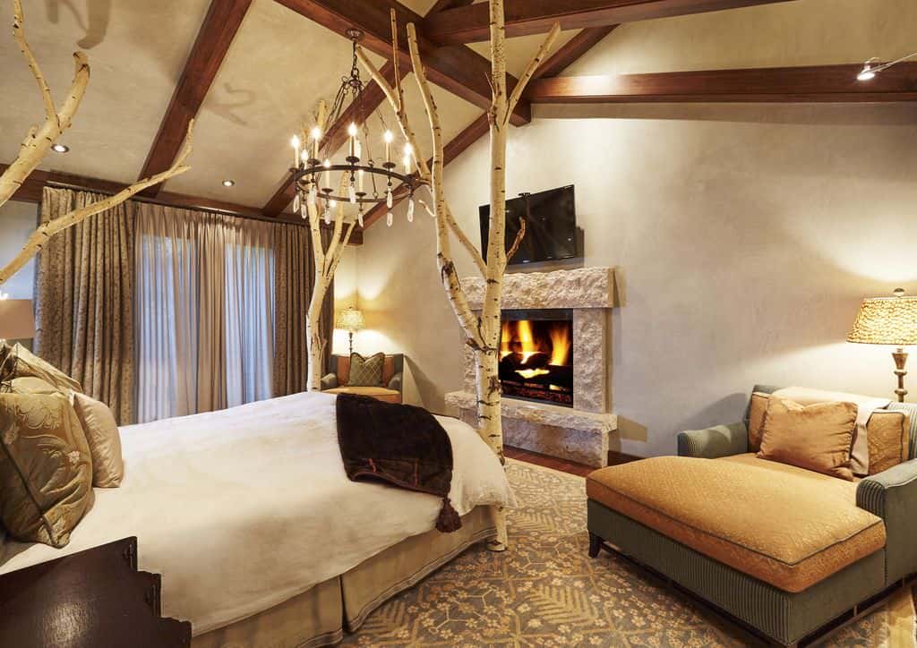 质朴的主卧室拥有一个奇妙的树床，由木梁天花板上悬挂的锻铁枝形吊灯照明。它正对着石砌壁炉，中间是沙发椅。
