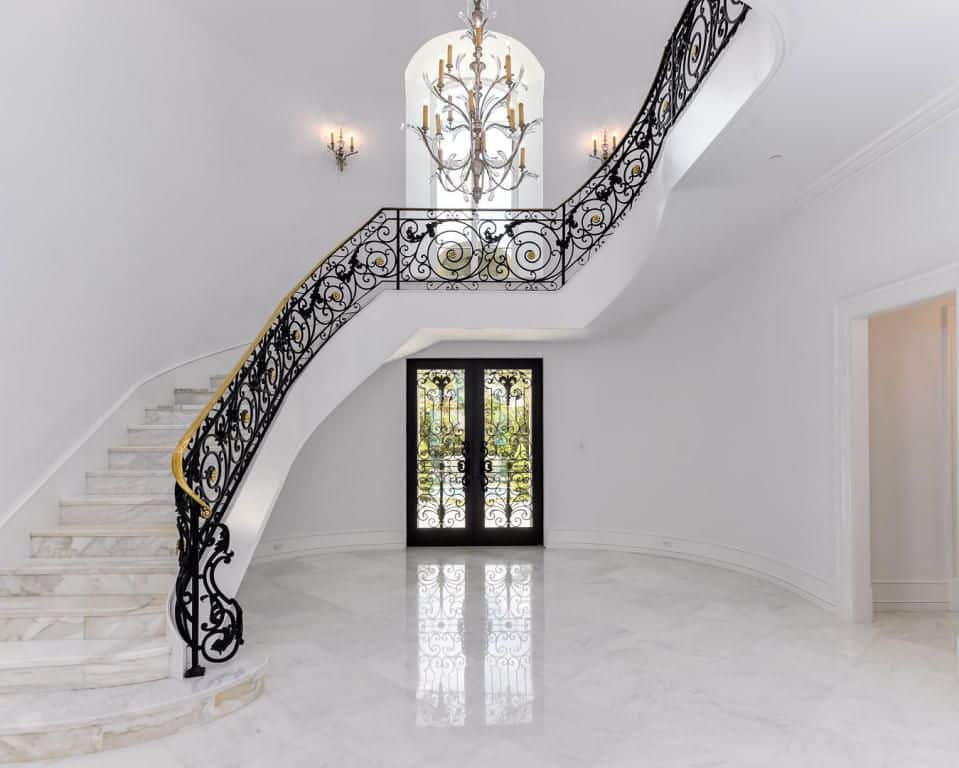 住宅入口有白色楼梯，大理石瓷砖地板和优雅的黑色栏杆，由一盏令人惊叹的吊灯照亮。