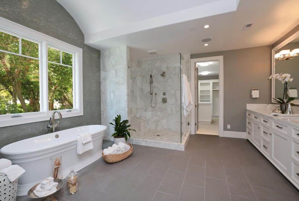 大型主要浴室，带有灰色墙壁和瓷砖地板。角落里有一个独立的浴缸和一个步入式淋浴。