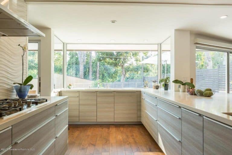 中性色调的厨房，浅灰色纹理的抽屉，嵌入式照明，硬木地板，和一个巨大的窗户，允许大量的阳光。