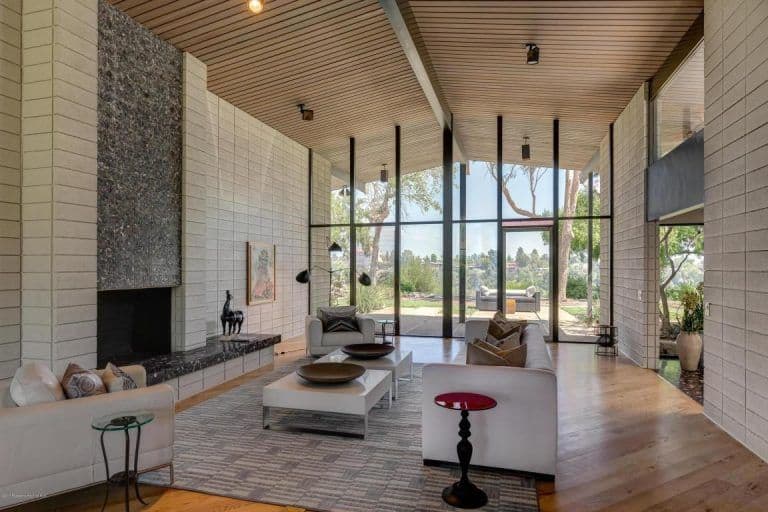 一间中世纪现代风格的客厅位于演员梅丽尔·斯特里普(Meryl Streep)拥有的帕萨迪纳(Pasadena)一栋经典建筑内，配有一套白色沙发、一座水磨石风格的燃木壁炉、两张咖啡桌和铺在硬木地板上的区域地毯。