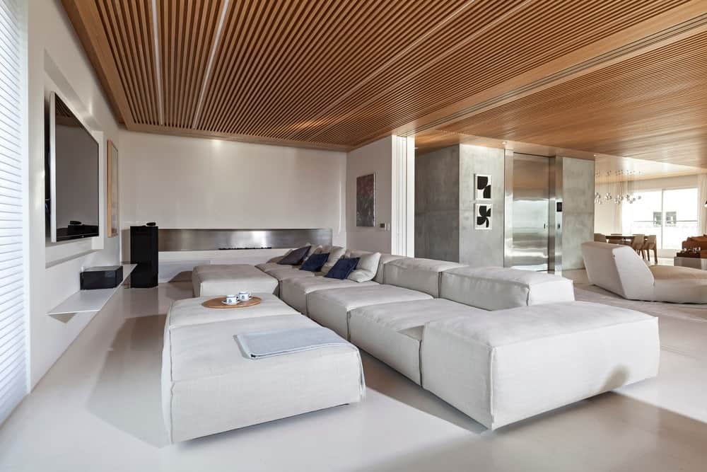 大型媒体室，白色墙壁和地板与白色沙发相匹配，在时尚的木质天花板下。