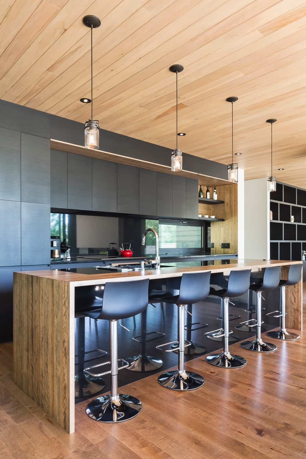 现代厨房，带夹层台面的长中心岛台。早餐吧的空间提供时尚的酒吧凳子设置在硬木地板上。漂亮的黑色橱柜为令人敬畏的厨房增添了风格。