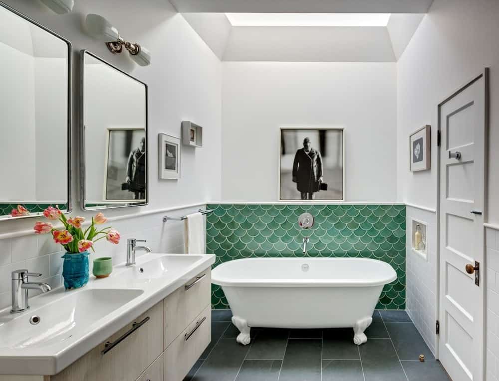 主浴室拥有一个带有绿色墙壁的独立浴缸。双水槽与白色墙壁搭配，带有时尚的墙壁艺术。图片来源:Francis Dzikowski/OTTO
