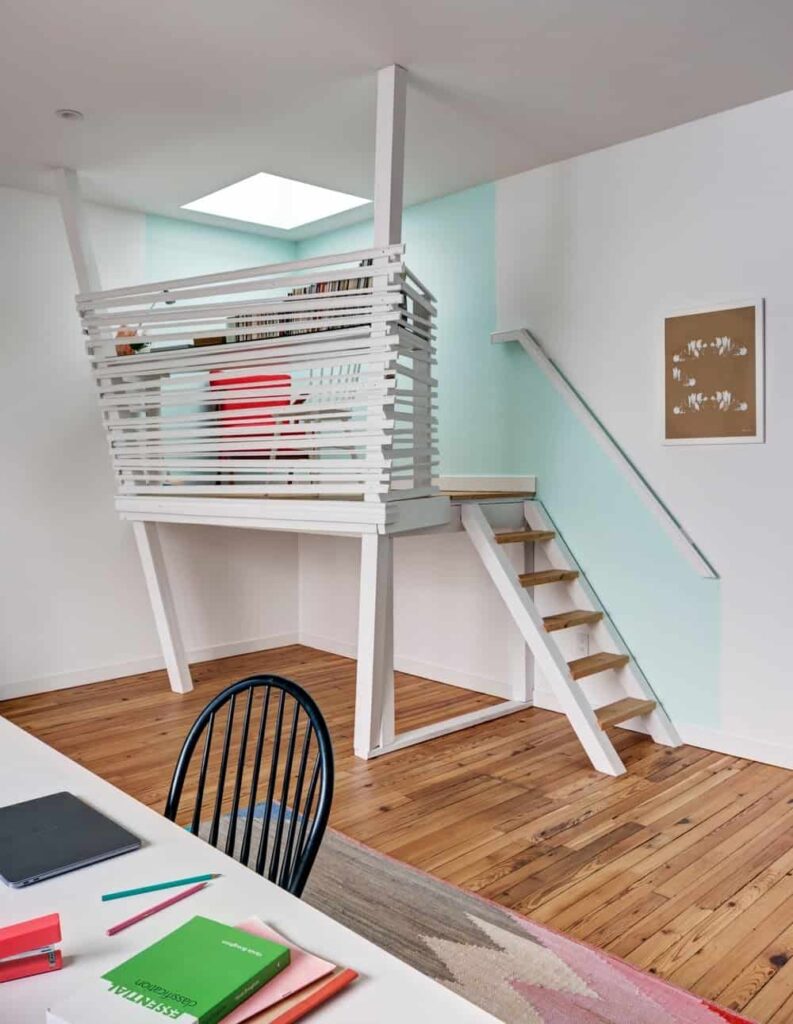 小型两层家庭办公室展示了一个开放式的楼梯，通往白色木栅栏包围的高架楼层，并通过天窗照明。