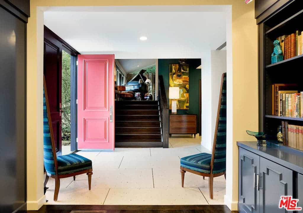 这个乡村风格的门厅以瓷砖地板、绿色墙壁、粉色门和一组带高靠背的蓝色椅子为特色。