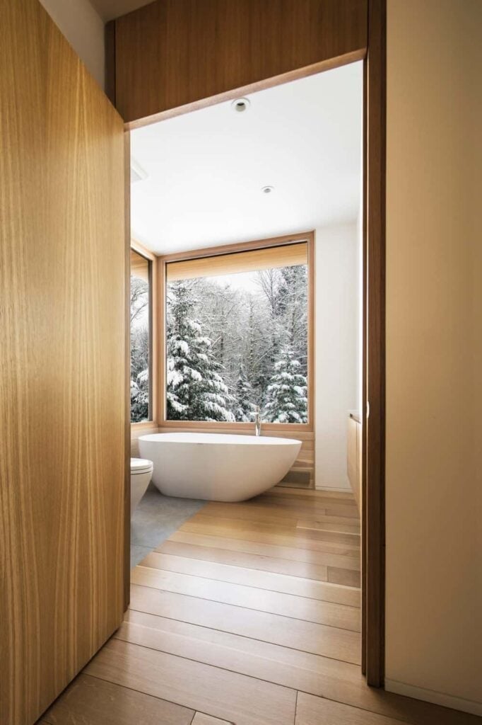 这间浴室设有一个独立的角落浴缸，靠近玻璃窗，提供室外景观的绝佳视野。