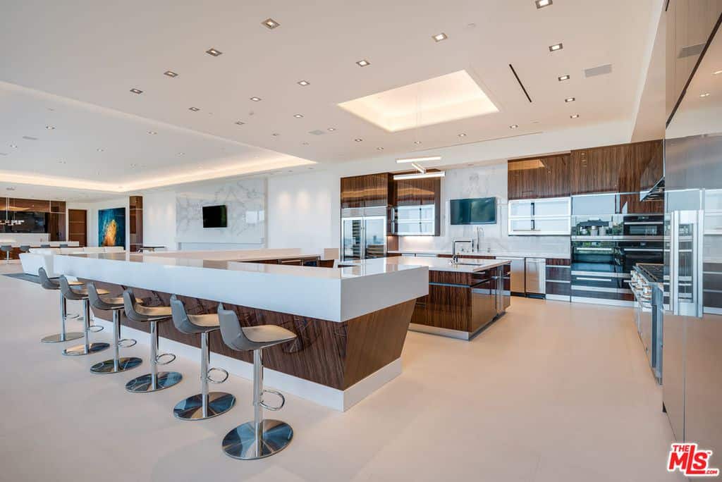 这个现代厨房非常漂亮。光滑的白色中心岛与层压细节提供了一个六个座位的早餐吧，而分散的天花板灯照亮了该地区。