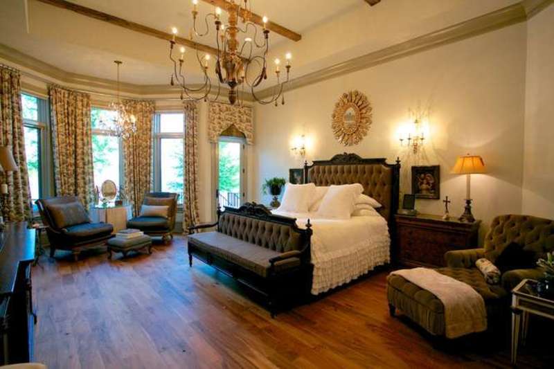 温暖的主卧室装饰有一面时尚的阳光反射镜，镜子安装在白色床上的簇绒床上。它包括一个配套的沙发，以及一个舒适的躺椅休息室和玻璃窗边的黑色椅子。
