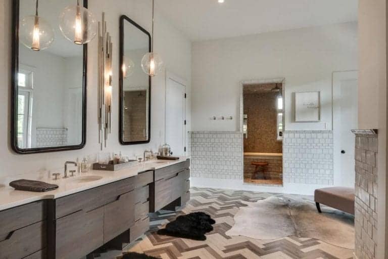 时尚的浴室拥有一个双水槽虚荣与玻璃球吊坠和一个独特的壁灯安装在黑框镜子之间。它有砖墙，人字形地板，上面铺着牛皮地毯。