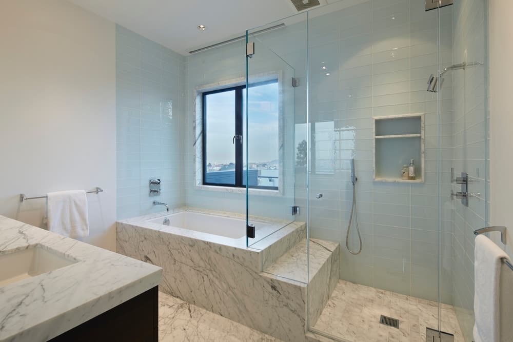 现代的白色浴室dropin的浴缸和步入式淋浴以及大理石台面和地板。图片来源:布鲁斯Damonte