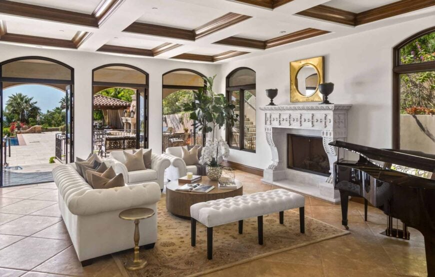 一间通风的客厅设有拱形玻璃窗和门，可通往庭院。它包括一个白色的切斯特菲尔德沙发和座椅，以及一个圆形的中心桌子和装饰有金色镜子的华丽壁炉。