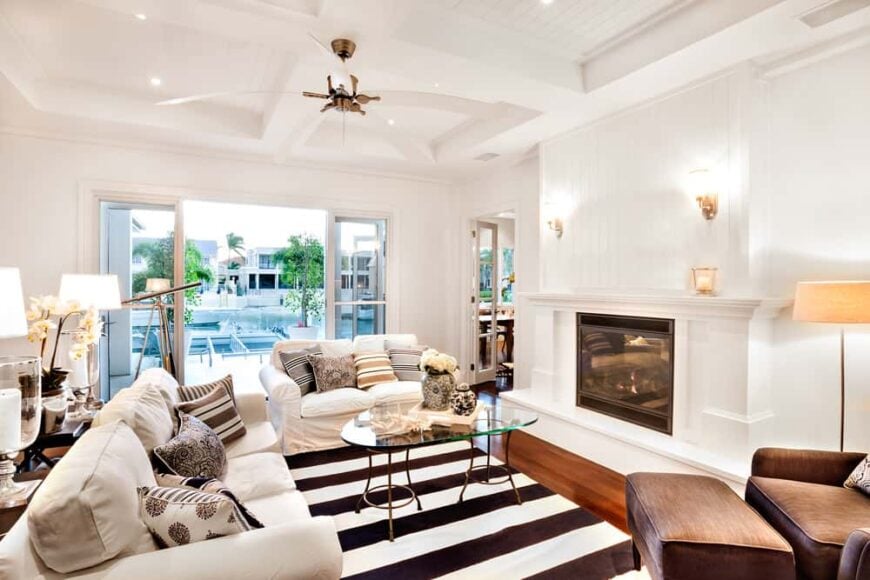 白色正式的客厅，配有舒适的沙发，壁炉前有一个玻璃顶部的中央桌子。墙上的灯饰看起来很可爱。