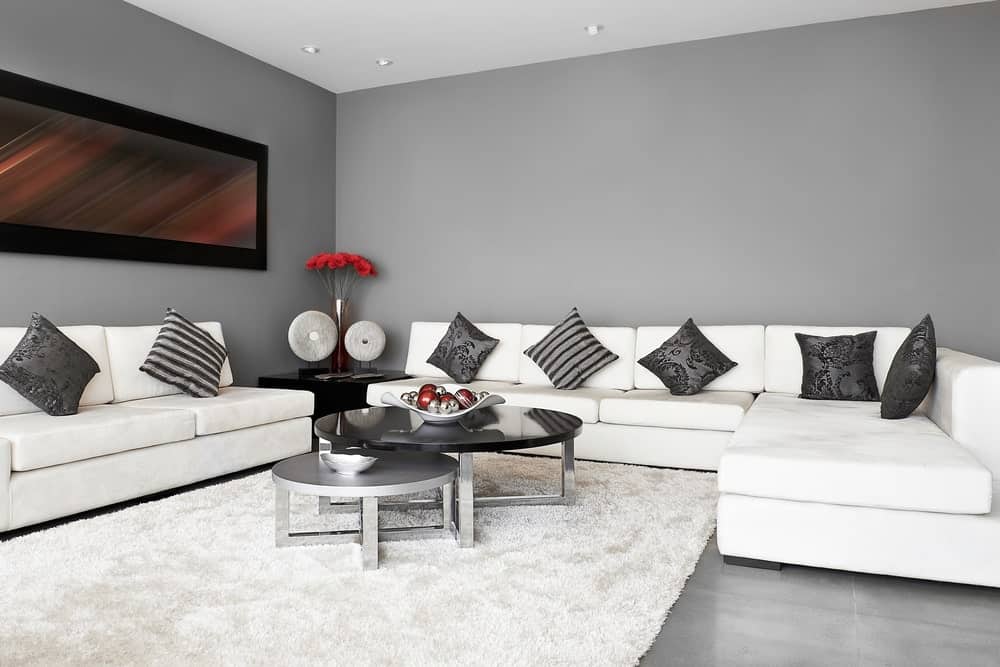 这间客厅有灰色的墙壁和灰色的地板，上面有白色的地毯。客房提供白色沙发和一张时尚的中央餐桌。