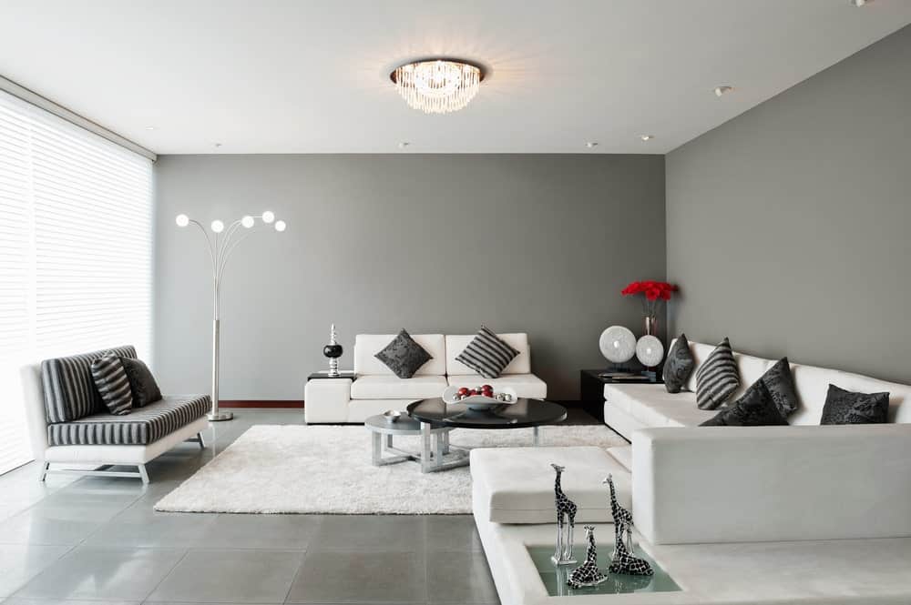 这间客厅配有一张白色沙发和一张时尚的中央桌子，上面铺着白色地毯，覆盖着灰色的瓷砖地板。