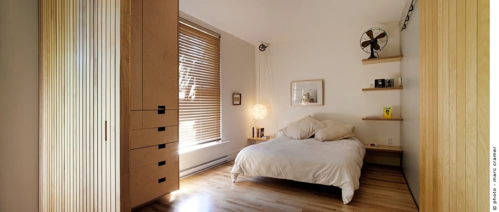 舒适的主卧室，木制浮动货架和衣柜。它以木制垂直板板墙和硬木地板为重点。