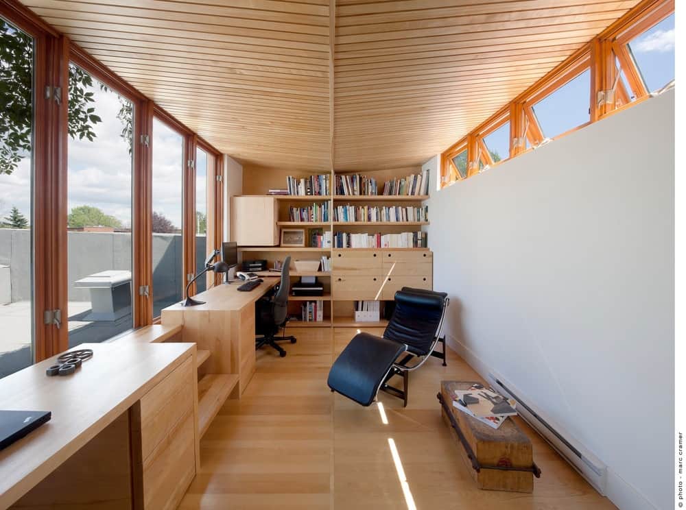 舒适的家庭办公室，通高的玻璃允许充足的自然光进入。它有一个木制书架和几张桌子，还有一个配有木桌的黑色躺椅休息室。