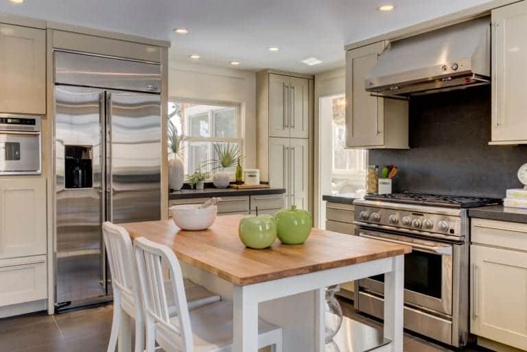 米白色的现代厨房，配有不锈钢电器和一个白色的厨房岛，木制表面和一对白色椅子。