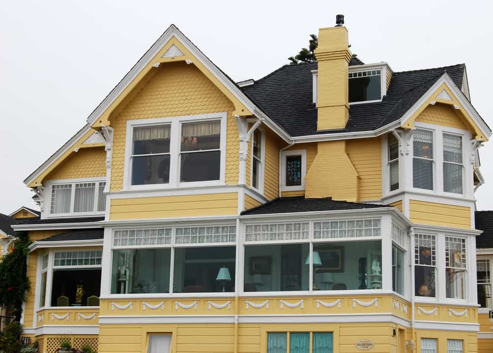 大型黄色维多利亚风格的房子，复杂的白色装饰与炭灰色的屋顶瓦形成了鲜明的对比。烟囱也是黄色的。