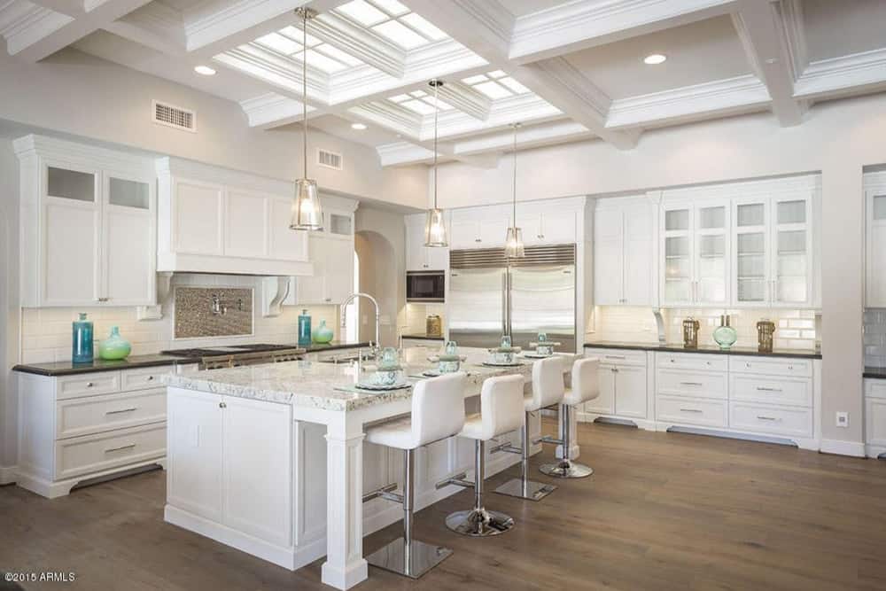 白色厨房，有一个时尚的早餐吧，由优雅的吊灯悬挂在格子天花板上。房间还设有硬木地板。