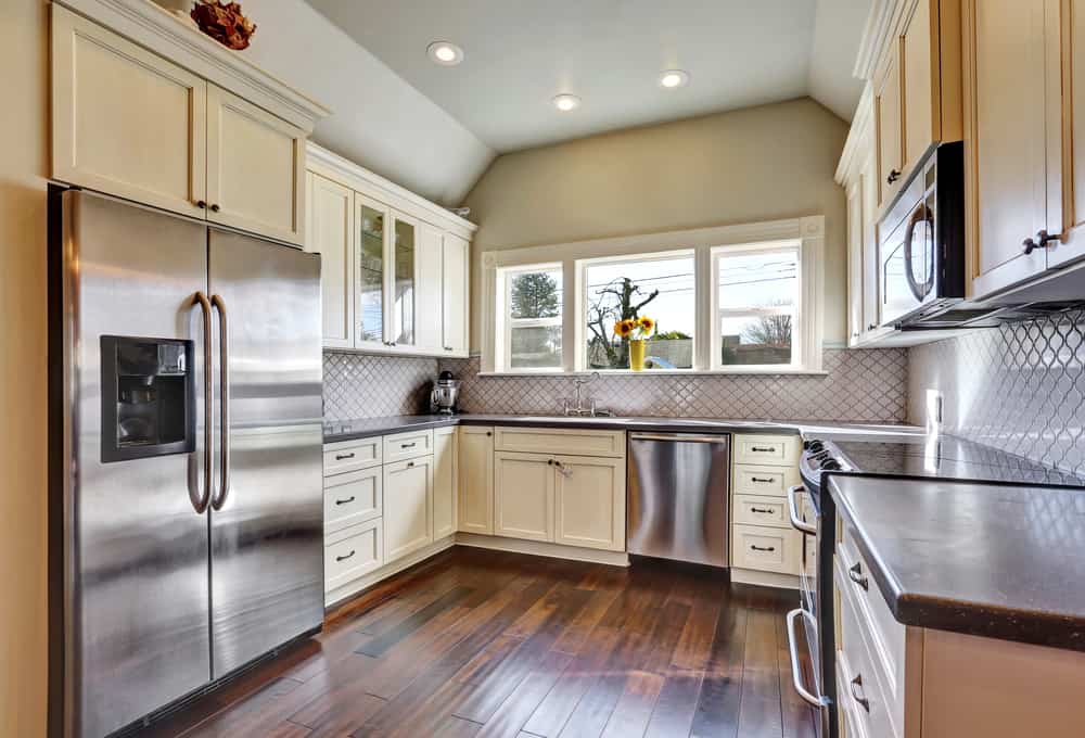 厨房房间内有一台内置不锈钢冰箱，铺有深色硬木地板和拱形天花板。