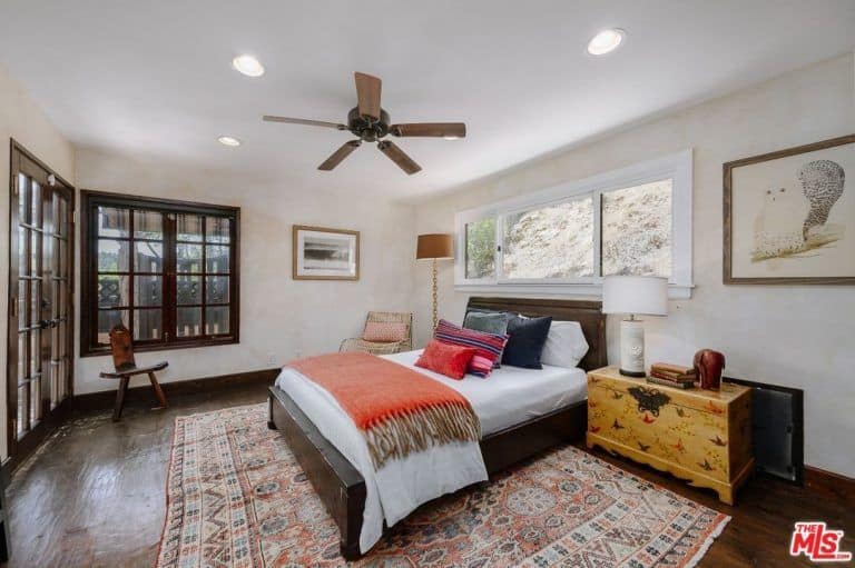 另一间卧室设有白色墙壁和硬木地板，以及经典的地毯和通往阳台的法式门。