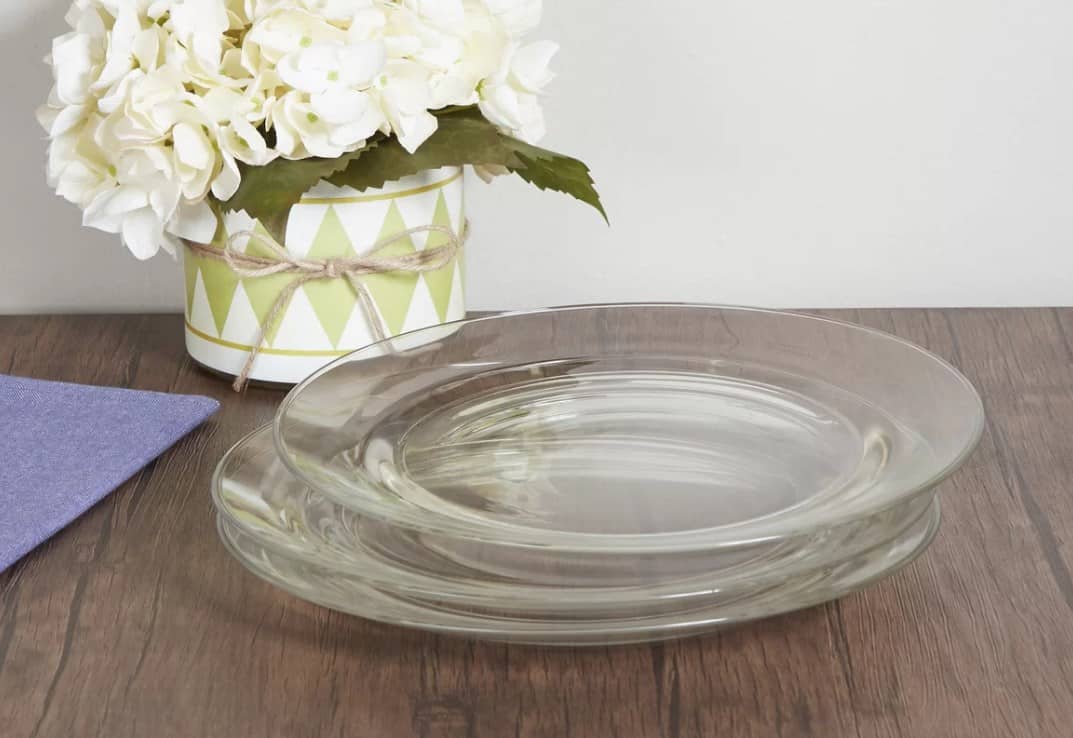Wayfair Basics 11英寸的透明玻璃餐盘放在木桌上，花瓶上放着白花。