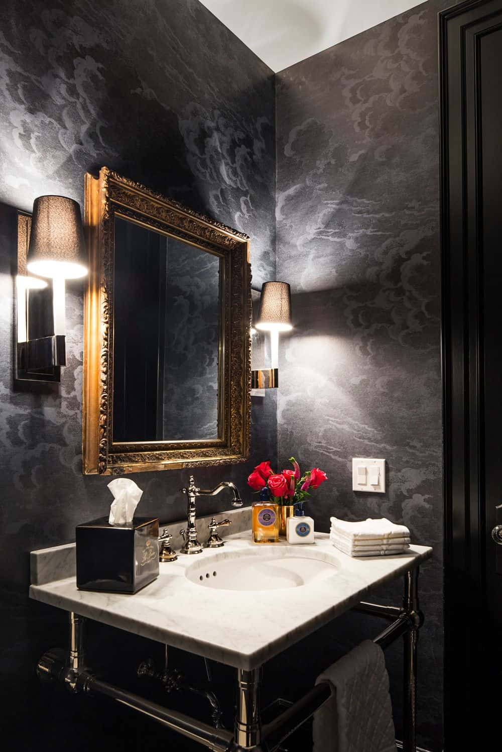 化妆室设有白色洗手台，周围环绕着优雅的黑色墙壁，由一对壁灯照明。图片来源:Erik Rotter