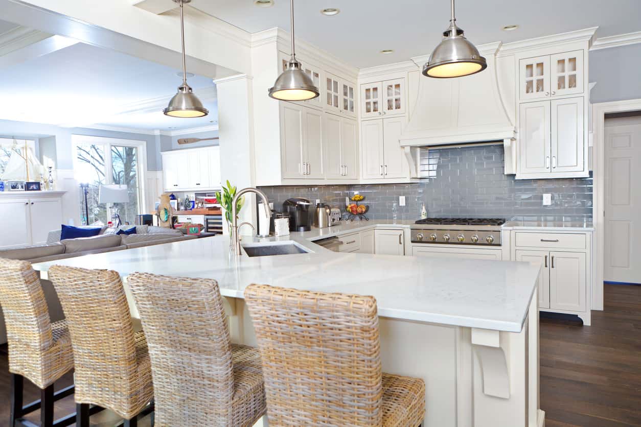 白色厨房与铬吊灯，蓝色后挡板，深色硬木地板和柳条早餐酒吧凳子。