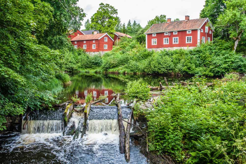 瑞典的几座红色外墙住宅，旁边是一条小河，周围是郁郁葱葱的植被。
