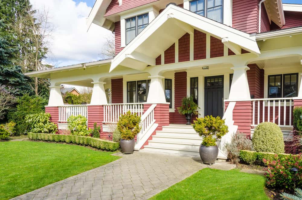 一个新的定制住宅的特写，红色的木材外观与大量的白色装饰形成对比。住宅包括大阳台和深灰色的前门。