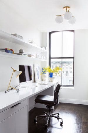 这是她的家庭办公室，有一张光滑的白色桌子，上面有架子和台灯。图片来源:Sarah Elliot