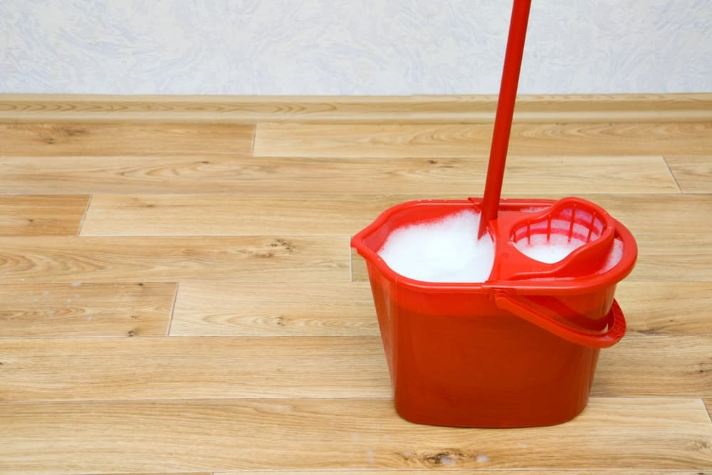一个红色的拖把桶和装满肥皂水的绞汁器放在木地板上。