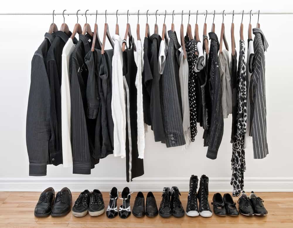 黑色和白色的衣服放在杆子上，不同的黑色鞋子放在木地板上。