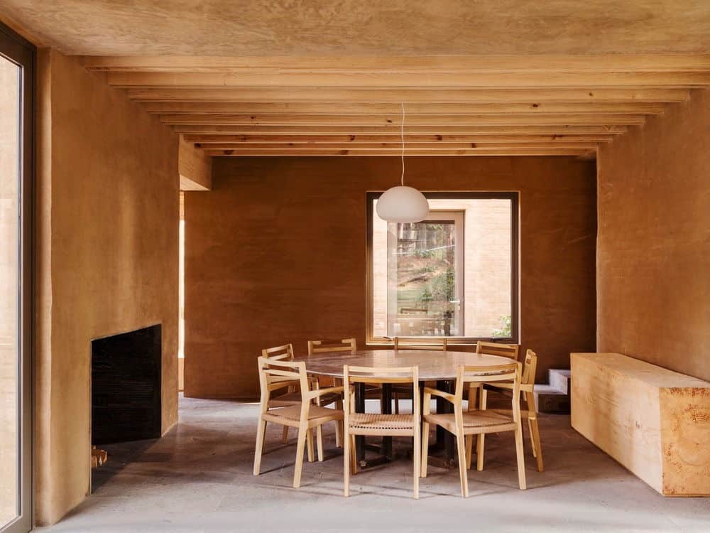 所有木材餐厅一个圆形餐桌和木制椅子之间的壁炉和内置的长椅上。是点燃的圆顶吊坠挂在木梁天花板。