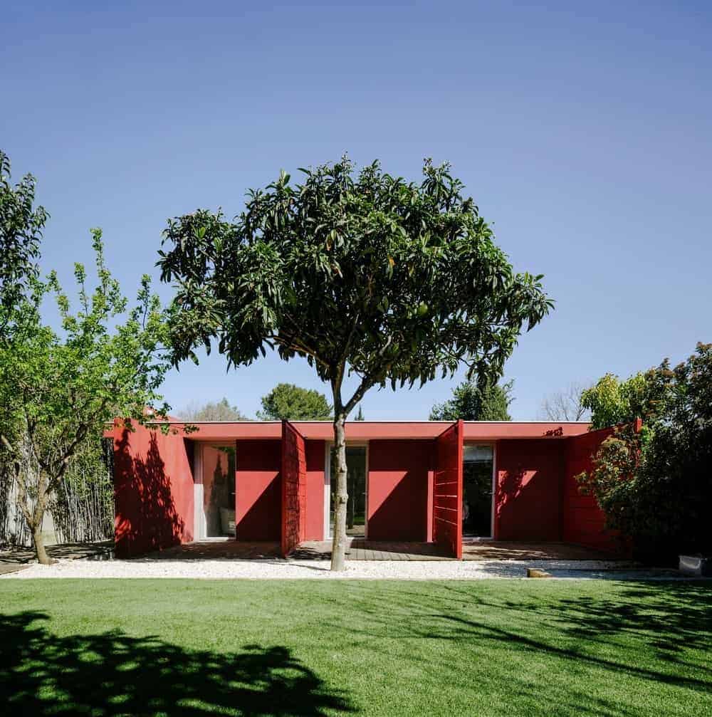 这座房子拥有红色的外观，周围环绕着健康的树木和维护良好的草坪区域。