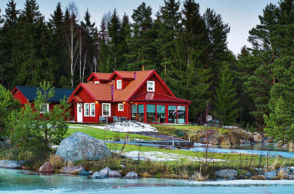 瑞典典型的红色海滨乡村住宅，阳光房被森林包围。红色的外观包括白色的装饰窗户和白色的前门。