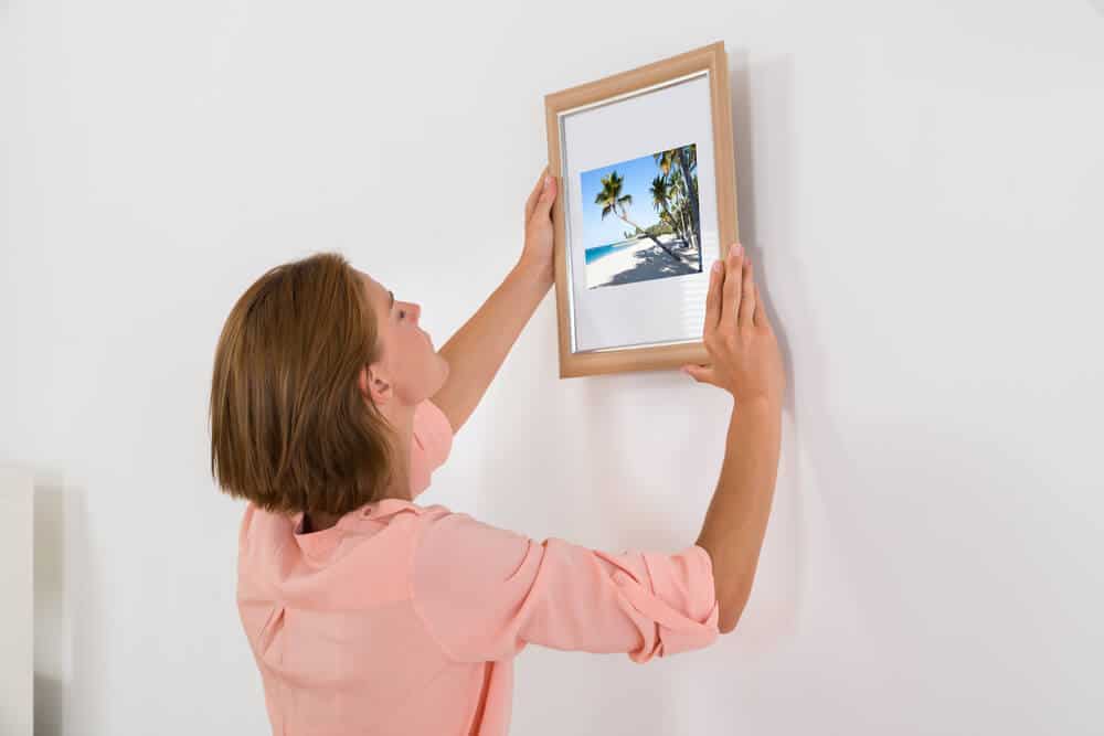 一个女人把一个木制的相框挂在墙上。