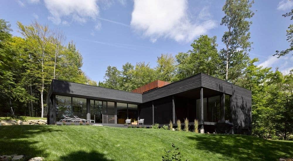 湖边的一栋黑色外观的现代住宅，坐落在维护良好的草坪上。