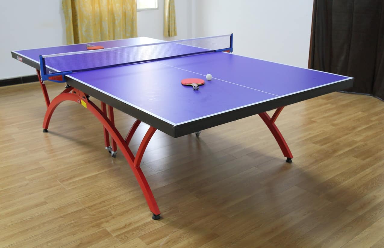 蓝色的室内乒乓球桌，红色的弯曲桌腿，放在木地板上。