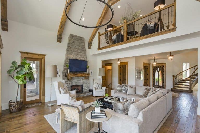 白色后卫椅子坐在两旁的石壁炉木制壁炉架下面这个客厅的电视和拱形的天花板和木板地板。