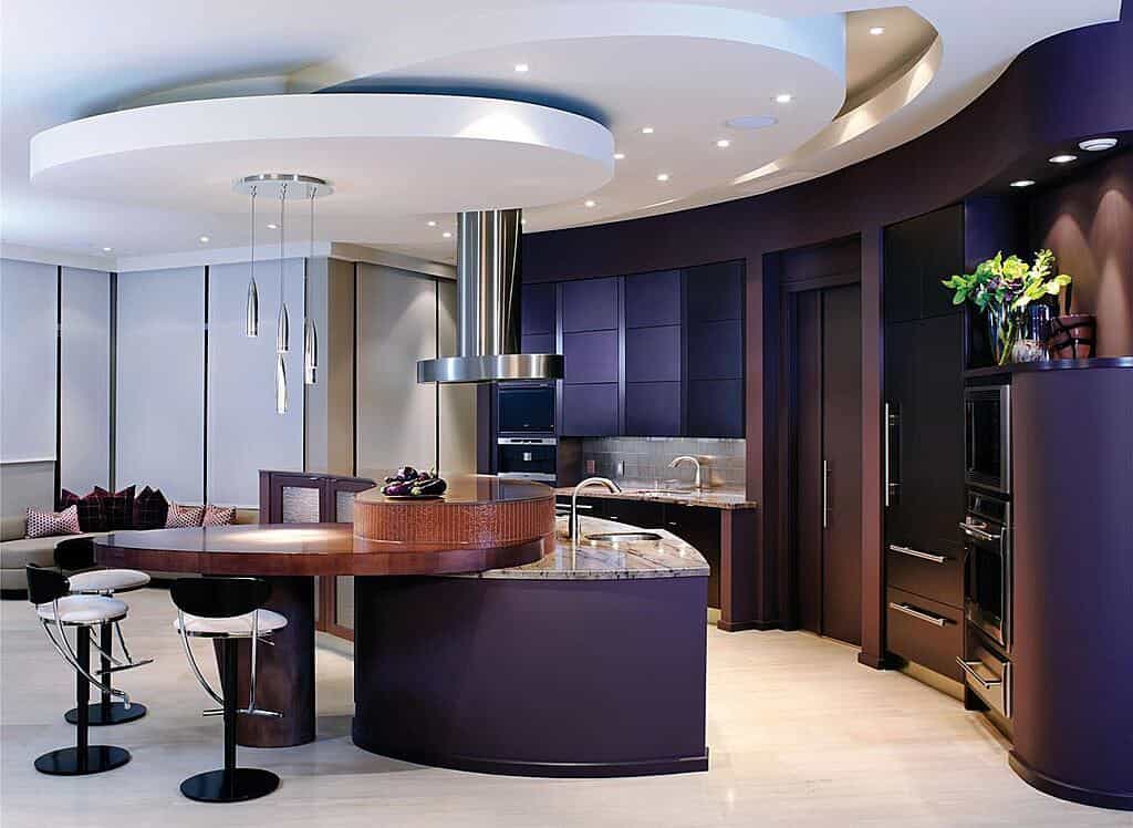豪华，现代的厨房沐浴在深紫色和木质调，大理石顶部的岛与扩展餐桌连接。