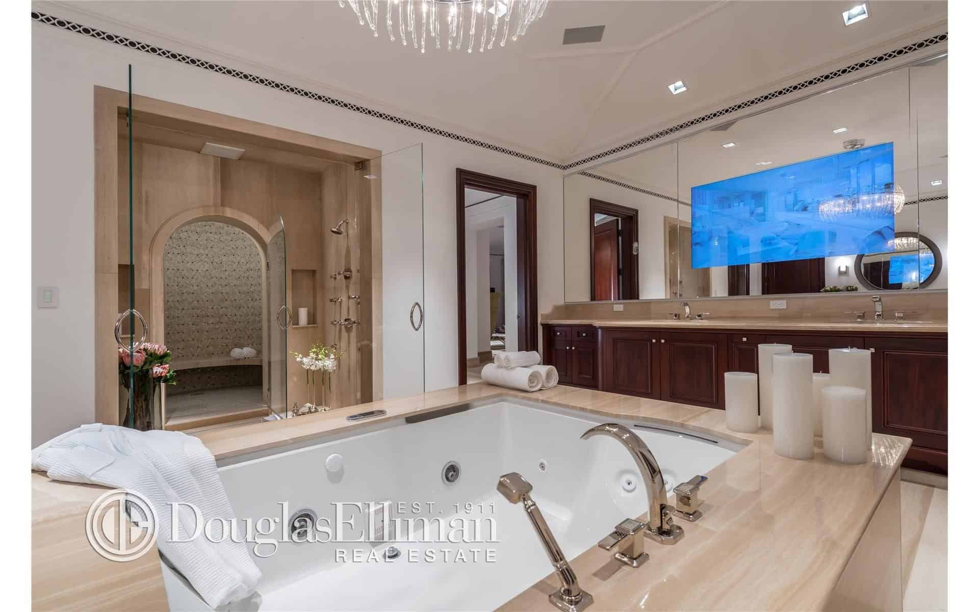 浴室的另一个视角聚焦于浴缸、吊灯和镜子上的宽屏电视。