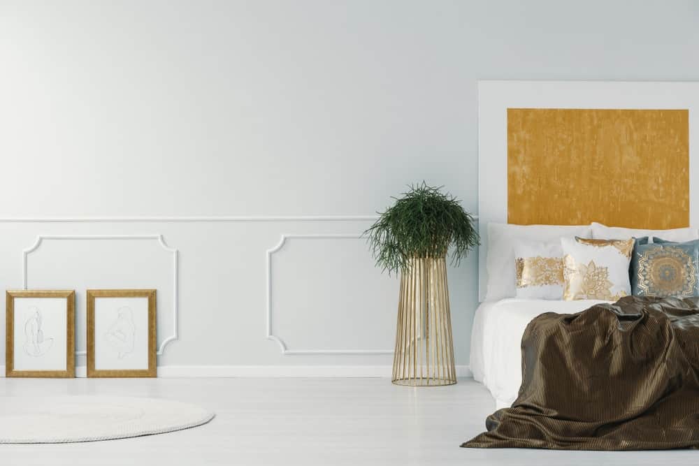 白色现代卧室与室内植物的金色植物架作为床头柜的选择。